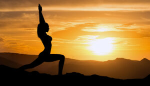 Silhouette of woman practicing yoga at sunrise.