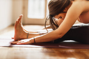 Relaxed young woman practicing yoga in Paschimottanasana pose at home.
