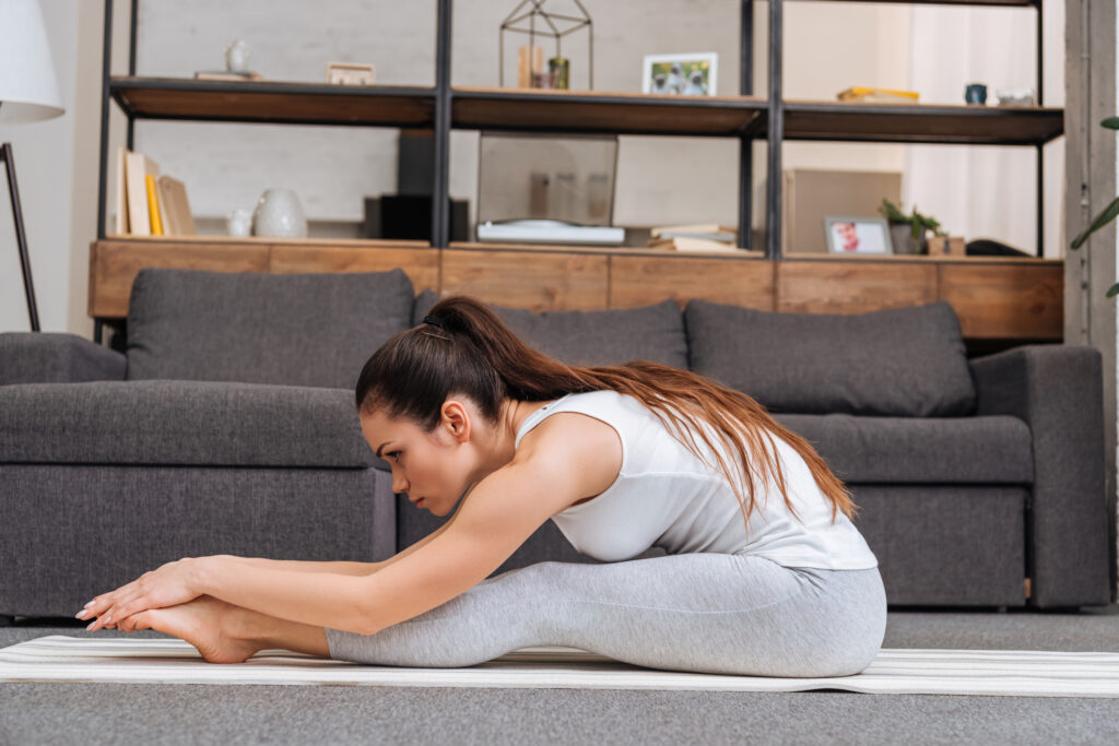 woman practicing seated forward fold pose on fitness mat at home in living room